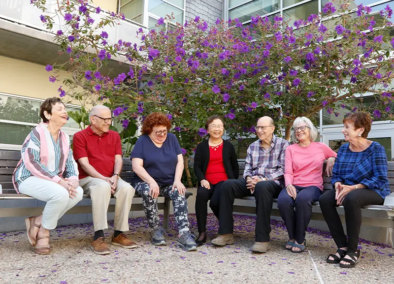 group of seniors sitting outside on a bench laughing and smiling