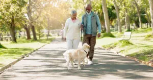 senior couple walking their dog outside on a paved trail