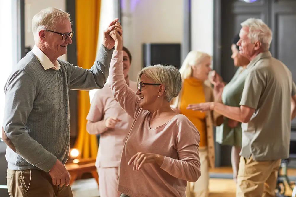 Seniors at Moldaw enjoy a lively ballroom dance class, holding hands and twirling during a social independent living event.
