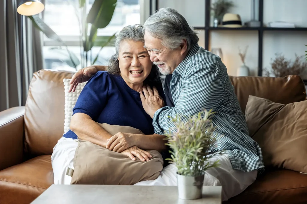 A senior couple laugh and embrace on a comfortable leather couch, showcasing the warm, homey environment enjoyed by Moldaw residents in independent living.